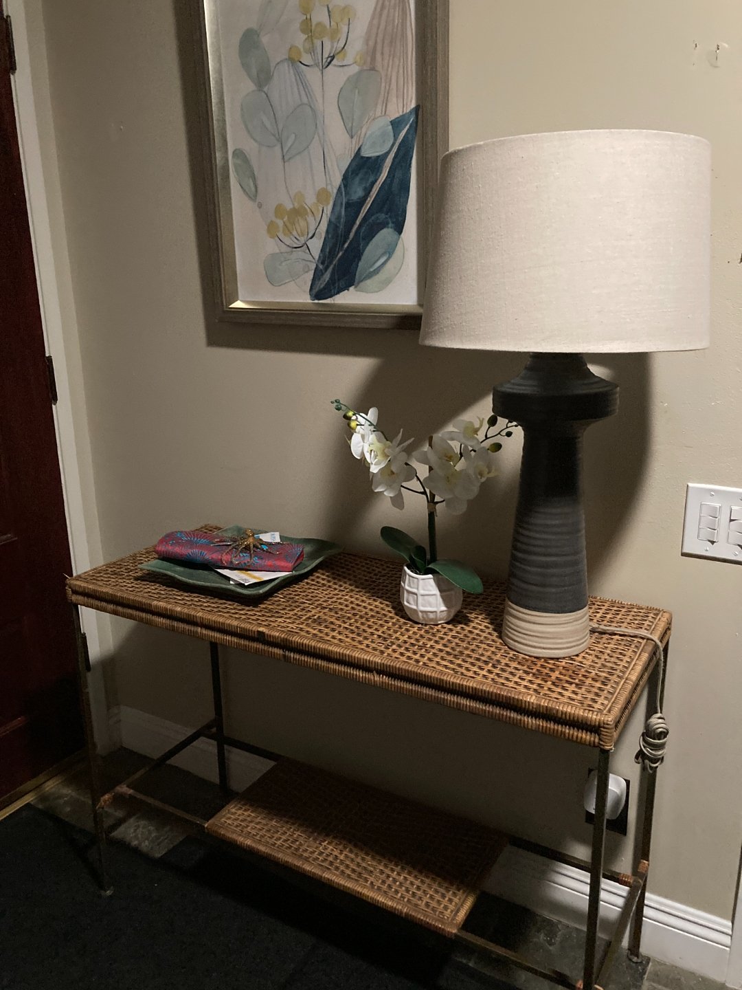 Rattan console table with orchid and lamp beside botanical artwork