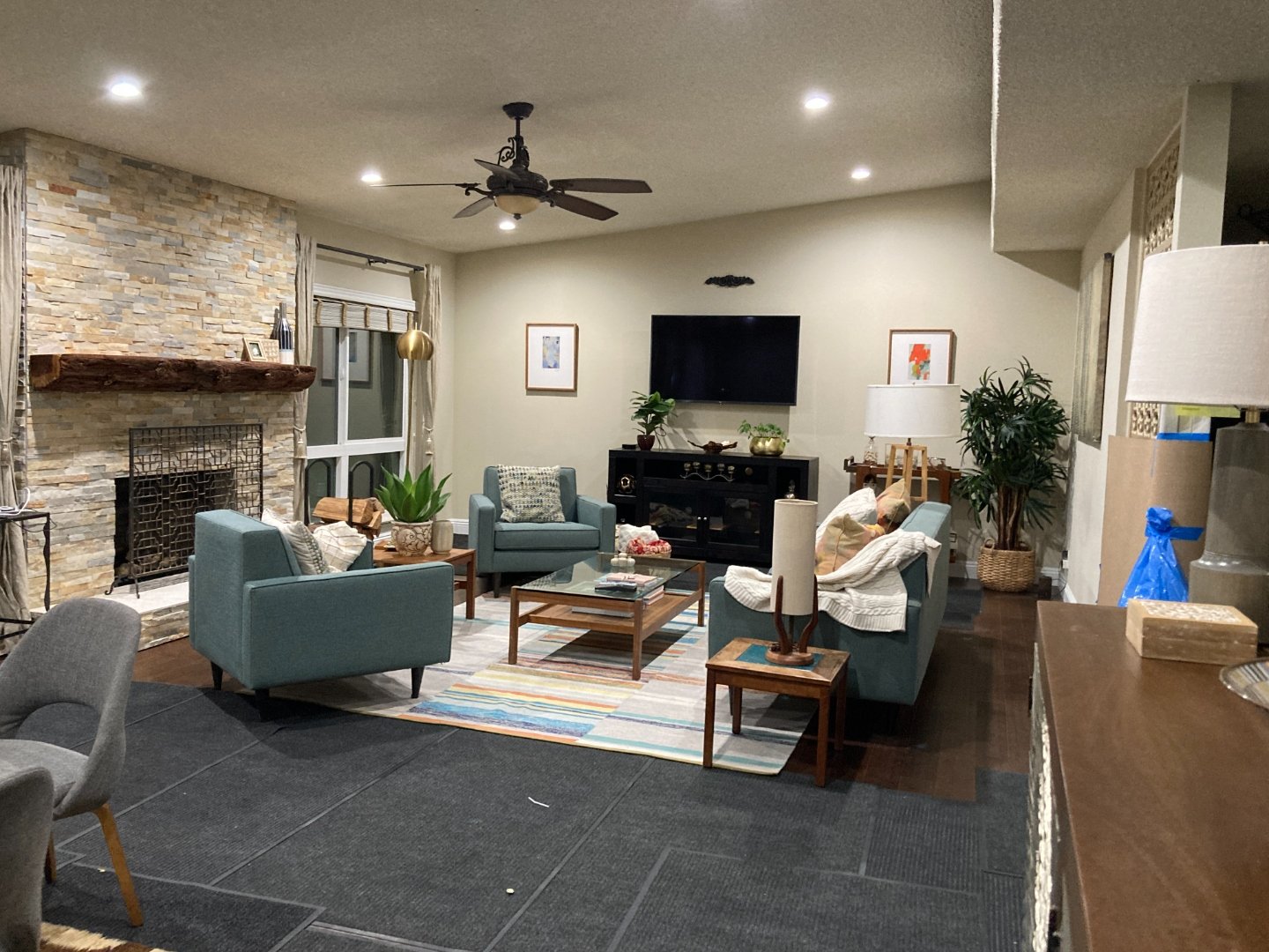 Family room with teal mid-century sofas, stone fireplace and ceiling fan