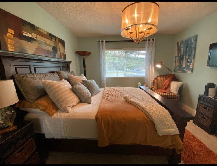 Master bedroom with styled dark wood bed, gold chandelier, layered bedding