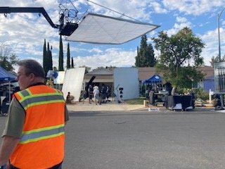 Production crew member in safety vest with camera crane and diffusion frame overhead