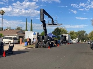 Wide shot of production crew with crane, tents, and equipment trucks on location